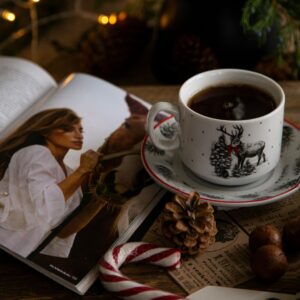 A cup of holiday-flavored tea sits next to an open magazine, a candy cane, and other holiday scenery.