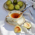 Image of a cup of tea and a plate of figs on a linen table spread.